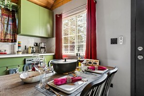 Un'area pranzo con un tavolo di legno apparecchiato per due persone, una pentola grande sul tavolo e una finestra con tende rosse.