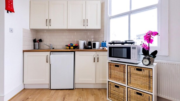 A kitchen with white cabinets, a refrigerator, a microwave, and wicker baskets on a white radiator.