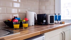 A kitchen with a coffee maker, a kettle, and a coffee machine. There are two glasses of orange juice on the counter.