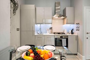 A modern kitchen with white cabinets, a stainless steel range hood, and a dining area with a glass table set for two.