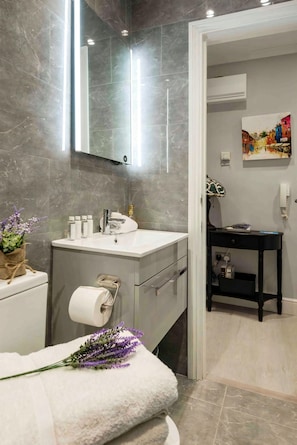 Une salle de bain moderne avec un mur en marbre, un lavabo blanc, un miroir, une serviette et une petite plante.