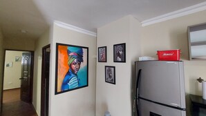 Una cocina con un refrigerador, un enfriador Budweiser y cuatro obras de arte enmarcadas en la pared.