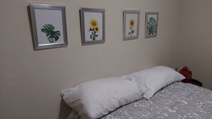 Un dormitorio con una cama, almohadas blancas y cuatro láminas enmarcadas con motivos botánicos en la pared.