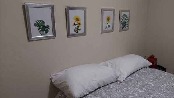 Un dormitorio con una cama, almohadas blancas y cuatro láminas enmarcadas con motivos botánicos en la pared.
