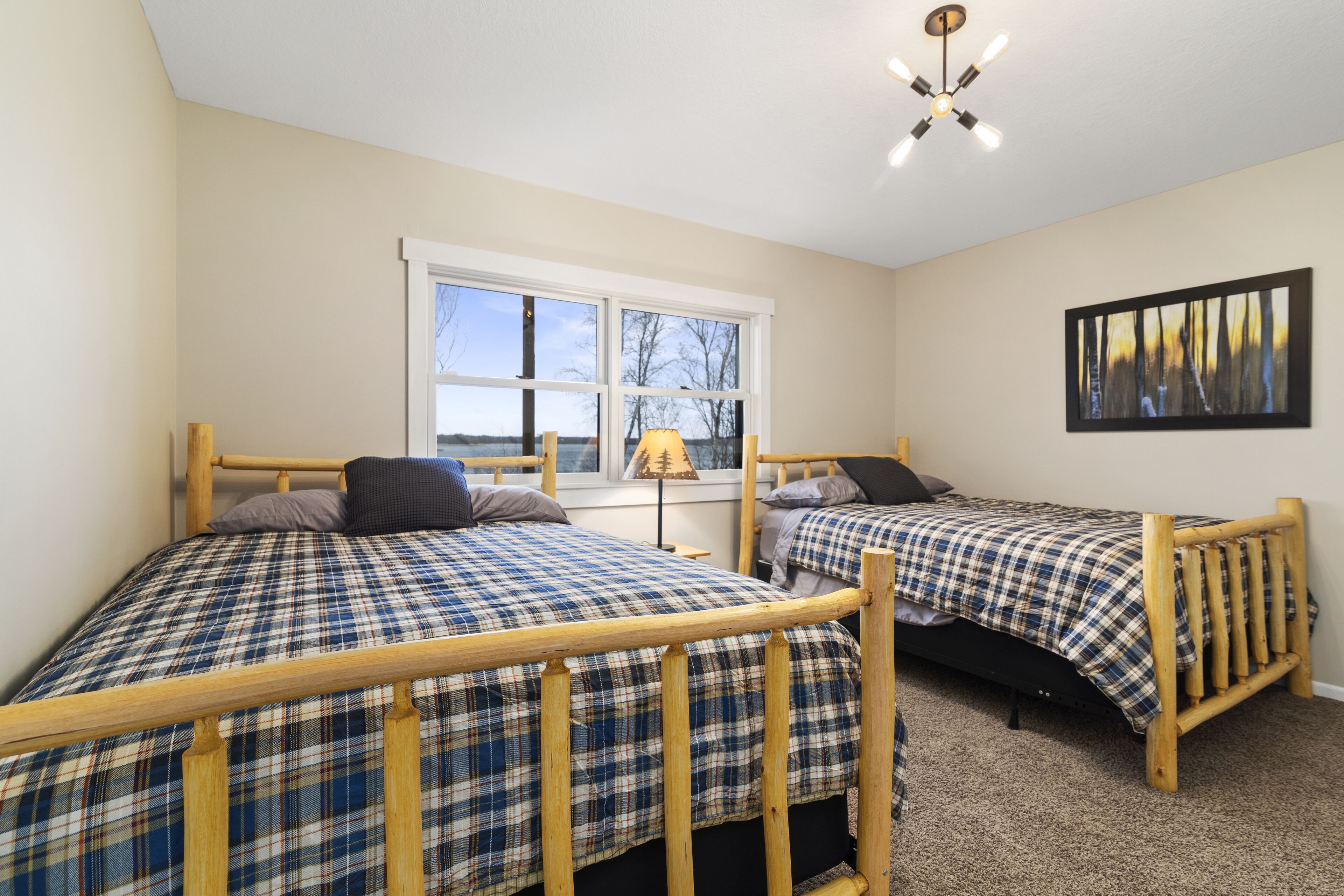 A bedroom with two wooden beds, a window with a view, a ceiling light, and a painting on the wall.