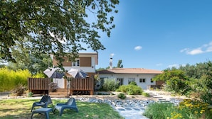 Una casa moderna de dos pisos con un patio, mobiliario exterior y un camino de piedra que lleva a la entrada.