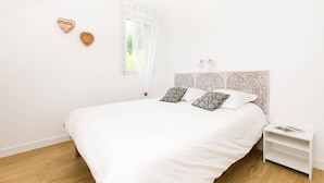 Un dormitorio minimalista con una cama grande, una mesita de noche y una ventana con cortinas translúcidas.
