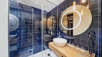 Un baño moderno con un espejo grande, un lavamanos redondo y una cabina de ducha de vidrio.