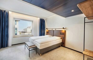 Ein modernes Hotelzimmer mit einem großen Fenster, einem Bett, einer Bank und einem Holzkopfende.