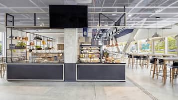 A modern cafe with a mezzanine level, open shelving with various items, and a seating area with tables and chairs.