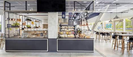 A modern cafe with a mezzanine level, open shelving with various items, and a seating area with tables and chairs.