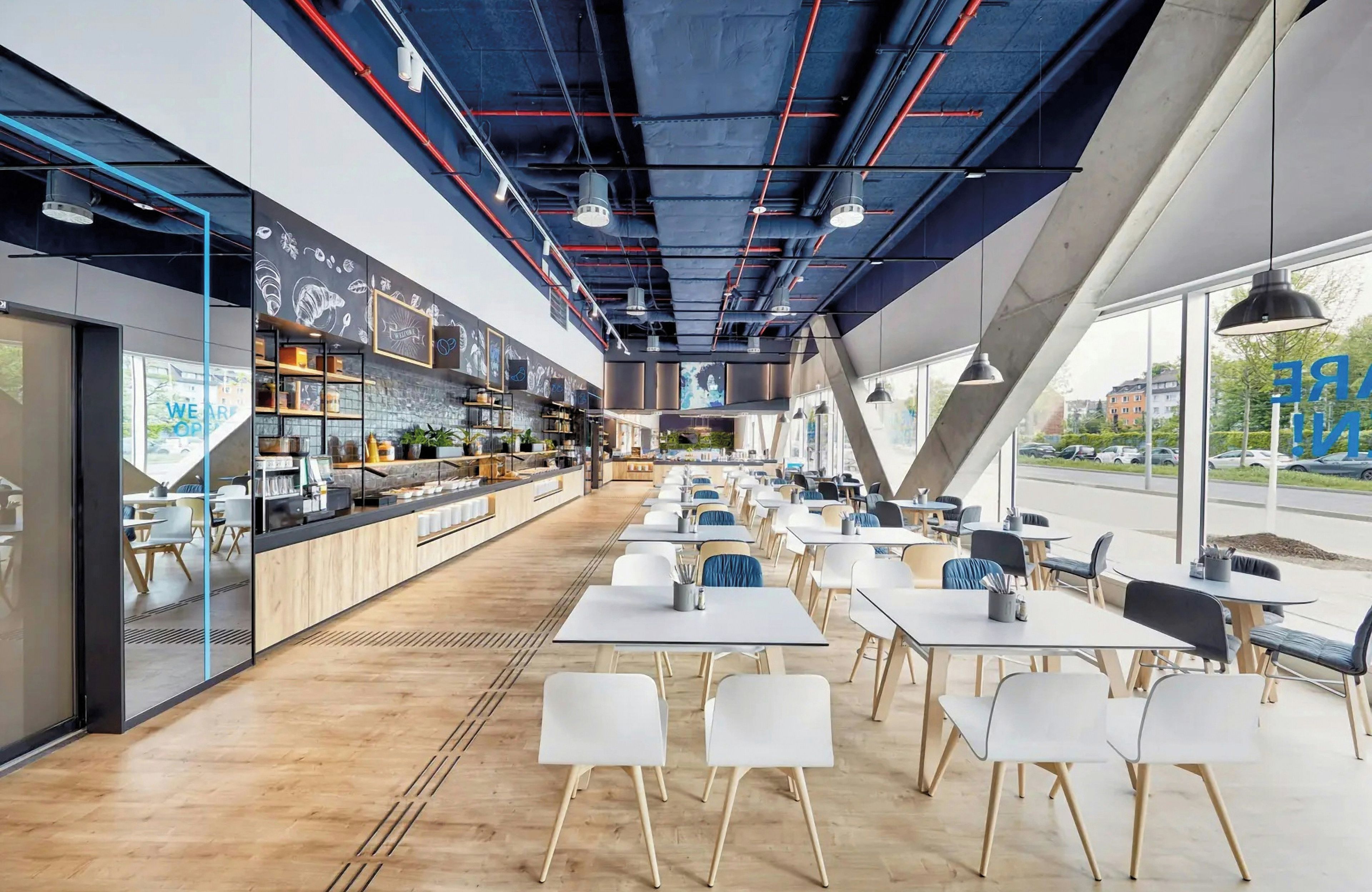 A modern cafe with a long counter, white chairs, and large windows.