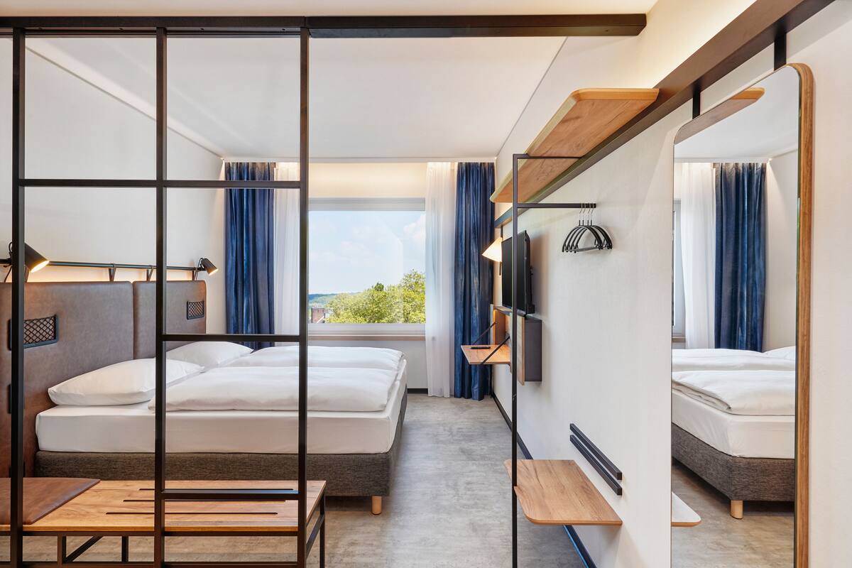 Ett modernt hotellrum med en stor säng, ett skrivbord, en TV och ett fönster med utsikt över omgivningarna.