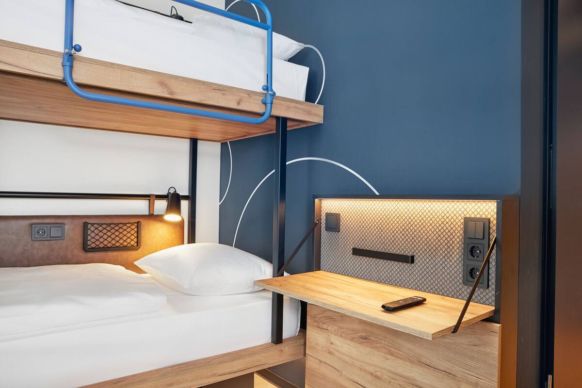 En våningssäng med ett skrivbord och en lampa, ett eluttag och en kontrollpanel på väggen.