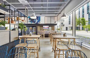 Ein modernes Café-Interieur mit Holztischen und -stühlen, einem großen Fenster und einem Automaten.