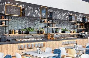 Un café moderne avec un mur recouvert d’un tableau noir, des étagères en bois et différents types de sièges.