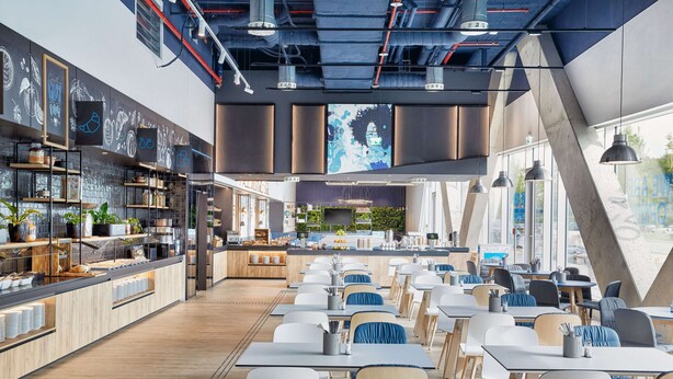 A modern restaurant with a long counter, seating area, and large windows. - H2 Hotel Düsseldorf City (Düsseldorf)