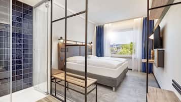 Ein modernes Hotelzimmer mit einem großen Bett, einer Sitzecke, einem an der Wand befestigten Fernseher und Blick ins Freie.