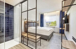 Une chambre d’hôtel moderne équipée d’un lit, d’un bureau, d’une chaise, d’une télévision et d’un balcon avec vue.