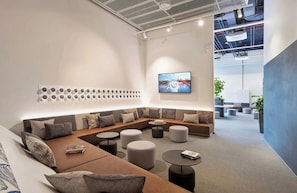 Un espace de détente moderne avec un canapé d’angle, des tables rondes et un téléviseur à écran plat fixé au mur.
