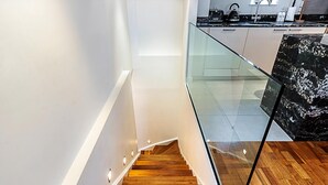 Een moderne keuken met glazen balustrade, houten trap en een marmeren aanrechtblad.