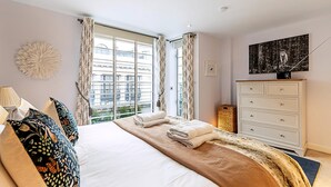 Een slaapkamer met een groot bed, een dressoir, een schilderij en uitzicht op gebouwen door het raam.
