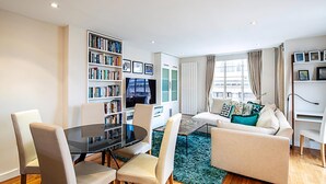 Een moderne woonkamer met een glazen eettafel, twee banken, een boekenkast en een televisie.