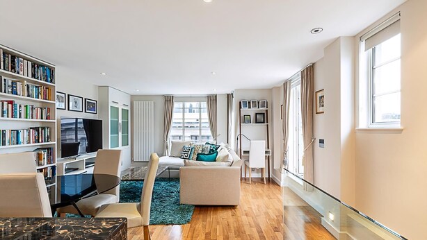 Een moderne woonkamer met een bank, fauteuils, een salontafel en een boekenkast.