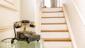 Un vieux téléphone, posé sur une table en verre dans un couloir avec un escalier.