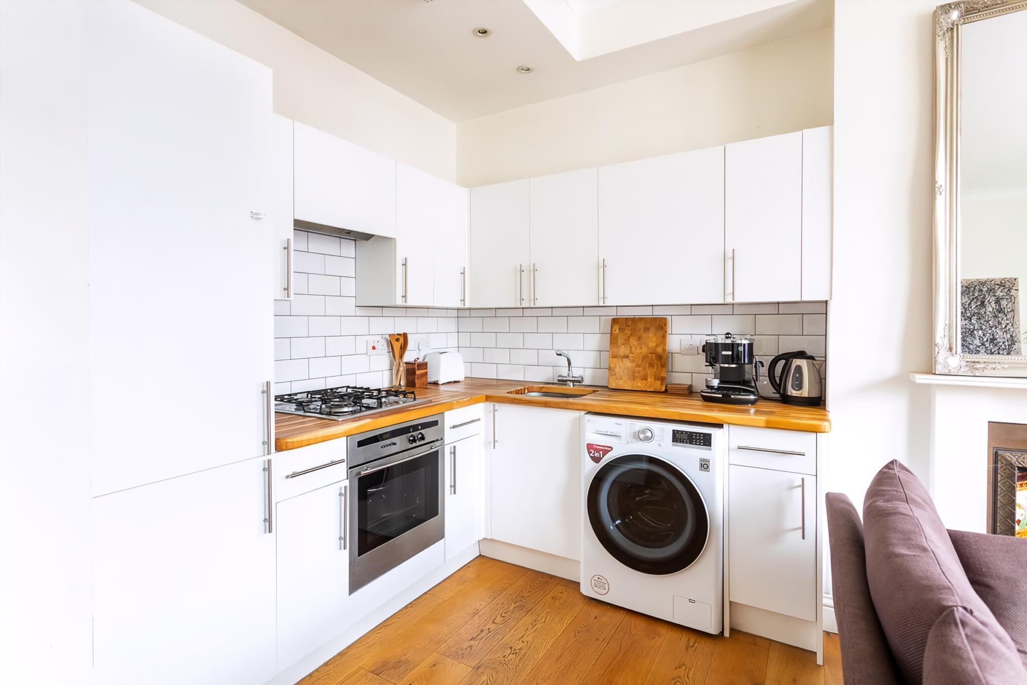 Una cocina compacta con armarios blancos, encimera de madera, lavadora y cafetera.