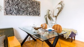 Un espace repas moderne avec une table en verre, un grand tableau abstrait et une plante en pot.