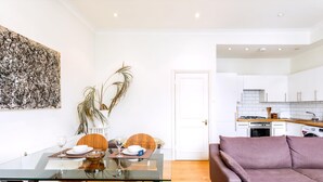 Un espace de vie moderne comprenant une table à manger en verre, un canapé, un coin cuisine et une porte donnant sur une autre pièce.