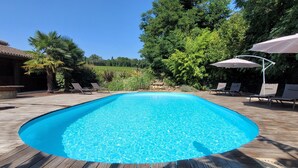 A rectangular swimming pool with a wooden deck surrounding it, two lounge chairs, and a large umbrella. - In the heart of Vineyards (LA REOLE)
