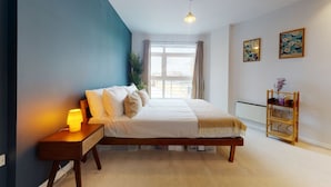 Une chambre à coucher comprenant un lit, une table de chevet, une lampe, une fenêtre et une étagère avec des objets décoratifs.