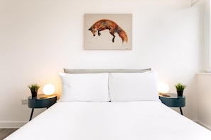 Un lit avec une literie blanche, deux tables de chevet avec des lampes et un tableau représentant un renard accroché au mur.