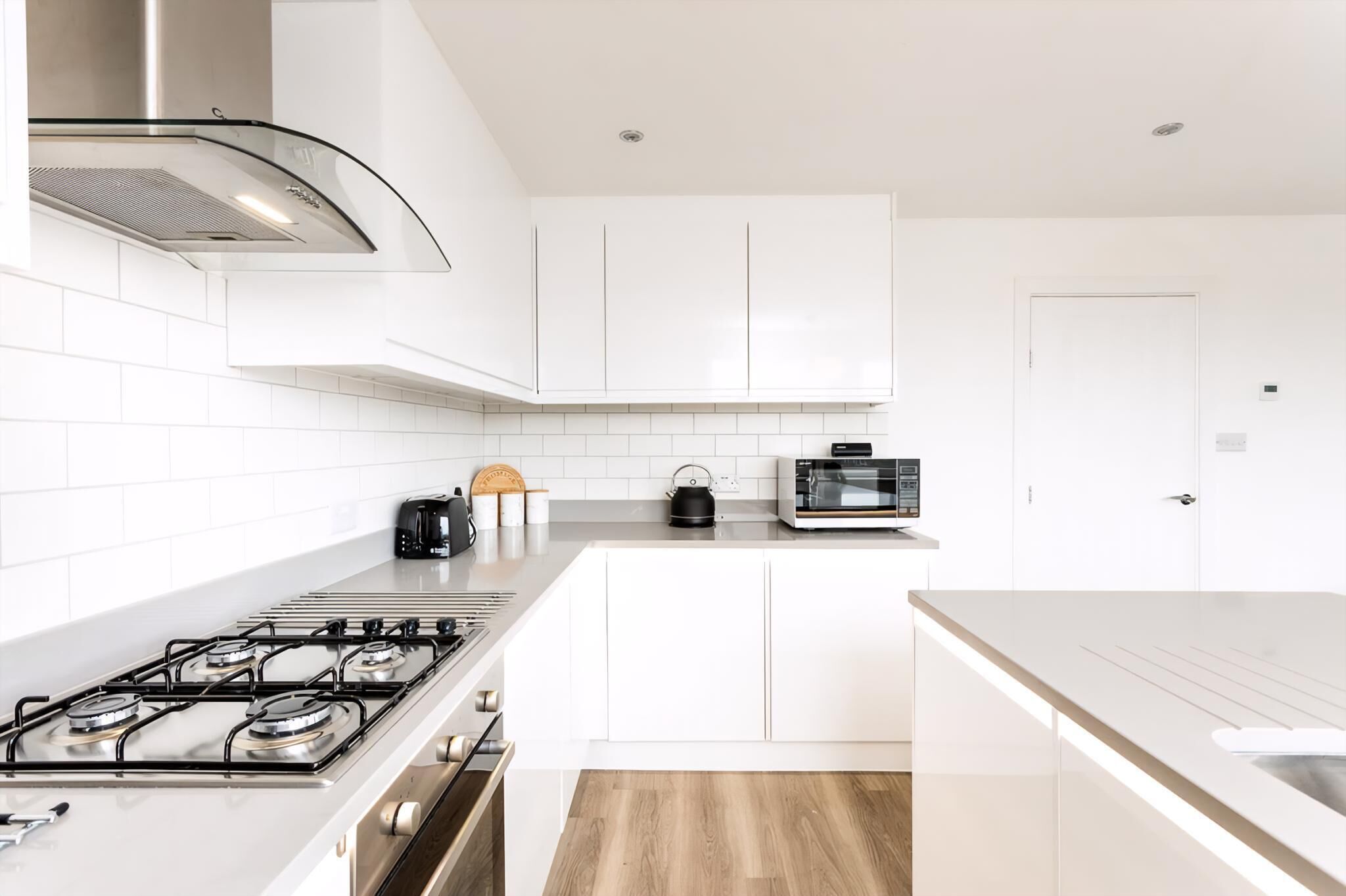 A modern kitchen with white cabinets, a gas stove, a toaster, and a kettle.