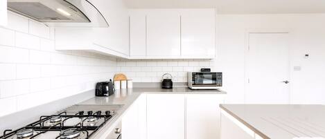 A modern kitchen with white cabinets, a gas stove, a toaster, and a kettle.
