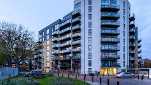 En moderne boligbygning med flere etager, altaner, anlagt have og parkerede biler.