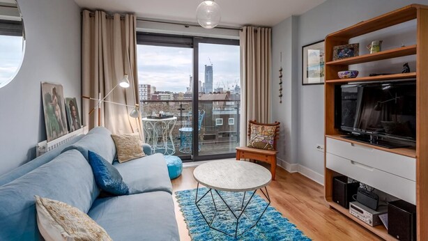 En moderne stue med sofa, rundt sofabord, tv-møbel og en balkon med udsigt over byen.
