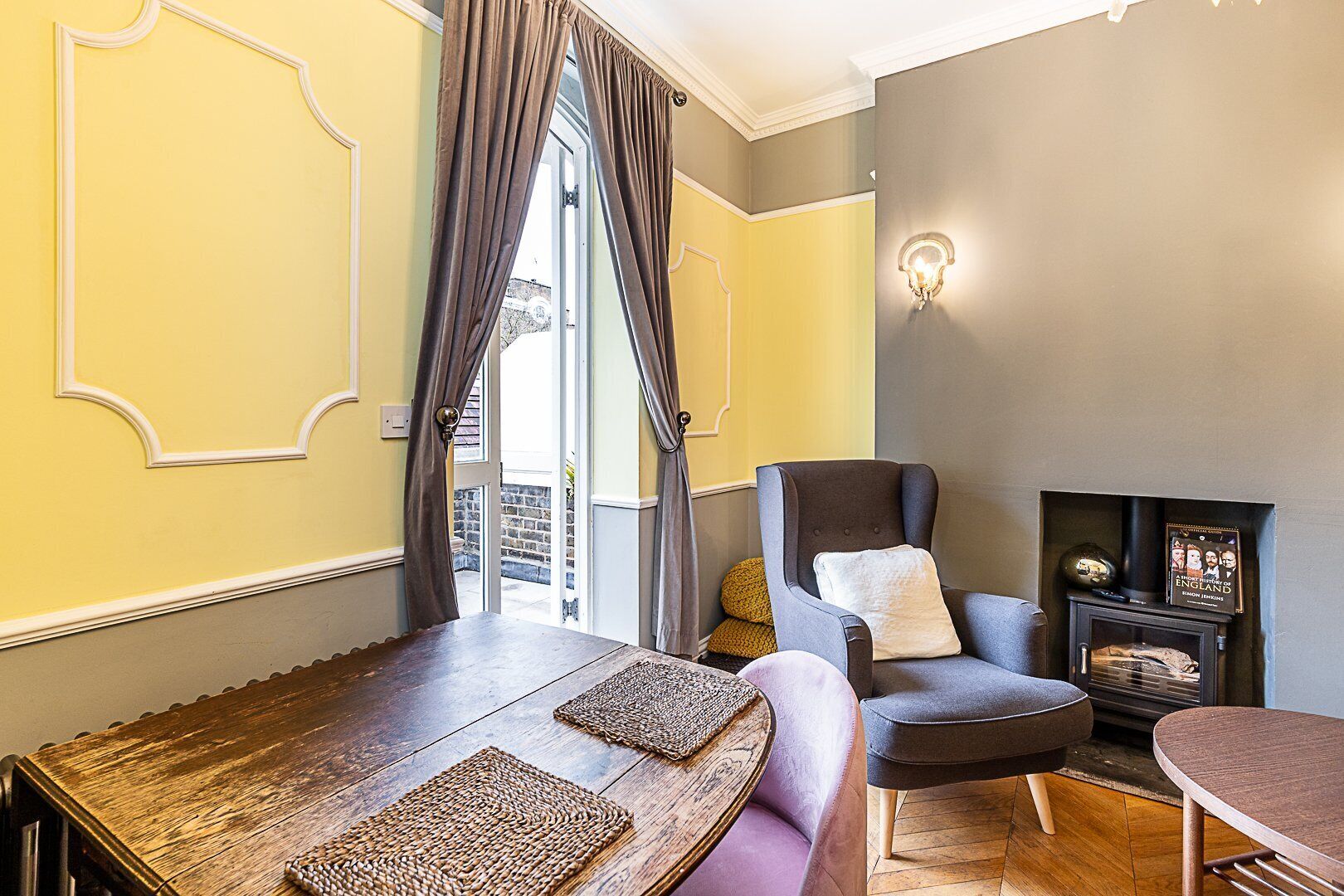 Een gezellige woonkamer met een houten tafel, een grijze fauteuil en een bank.