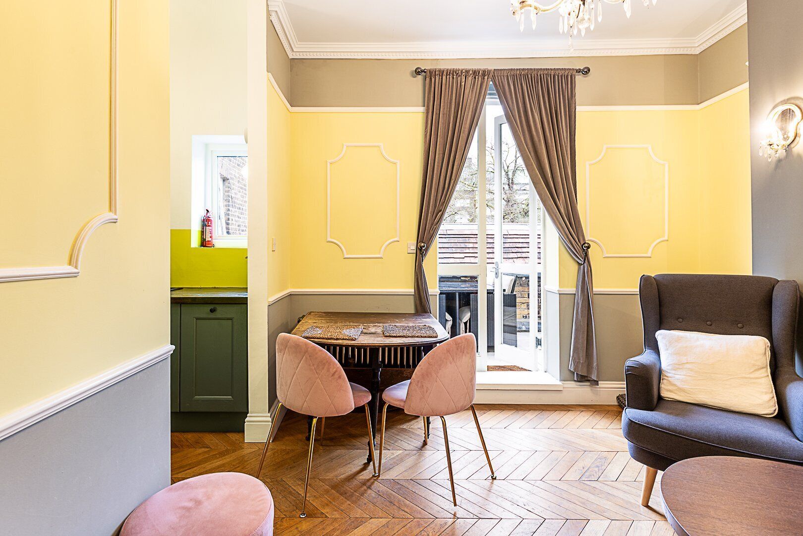 A room with a dining table, two chairs, a sofa, and a view through a glass door.