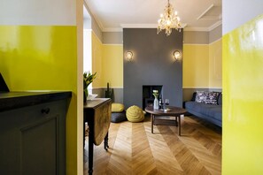 Ein Wohnzimmer mit Fischgrätparkett, Kamin, Sofa und einer Chandelier.