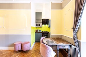 Eine kompakte Küche mit modernen Geräten, ein Essbereich mit Tisch und Stühlen sowie ein Flur, der zum Schlafzimmer führt.