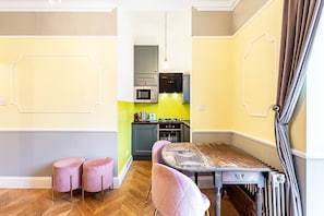 A compact kitchen with modern appliances, a dining area with a wooden table and pink chairs, and a radiator.