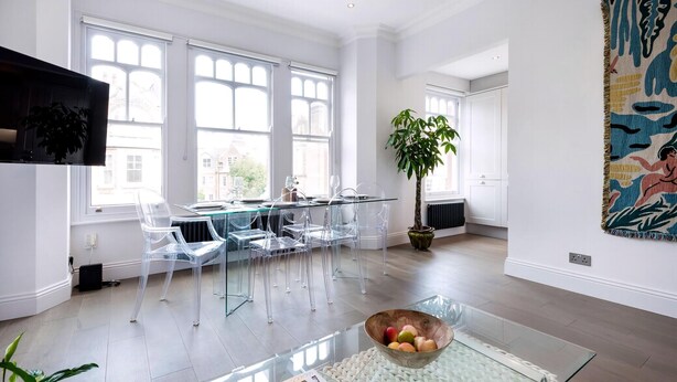A modern dining area with a glass table, clear chairs, and a large window. - Modern and Bright Highgate Gem (London)
