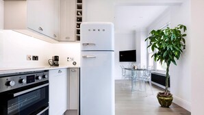 A modern kitchen with a white refrigerator, double oven, and a dining area with a plant. - Modern and Bright Highgate Gem (London)