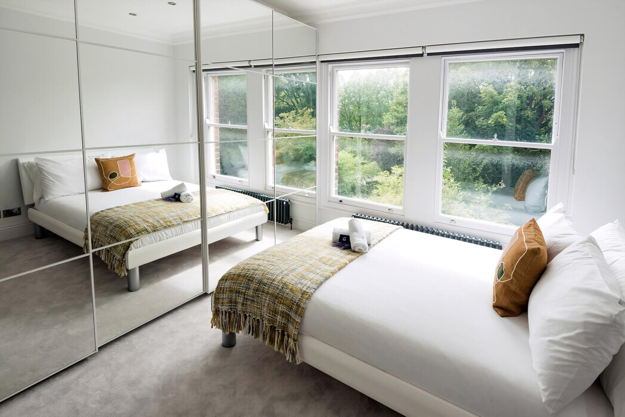 A modern hotel room with a large mirror, two beds, and a view of greenery outside.