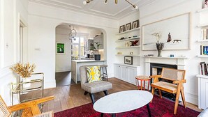 A spacious living room with a red rug, a white table, and two wooden chairs. - Stunning Maida Vale Apartment (London)