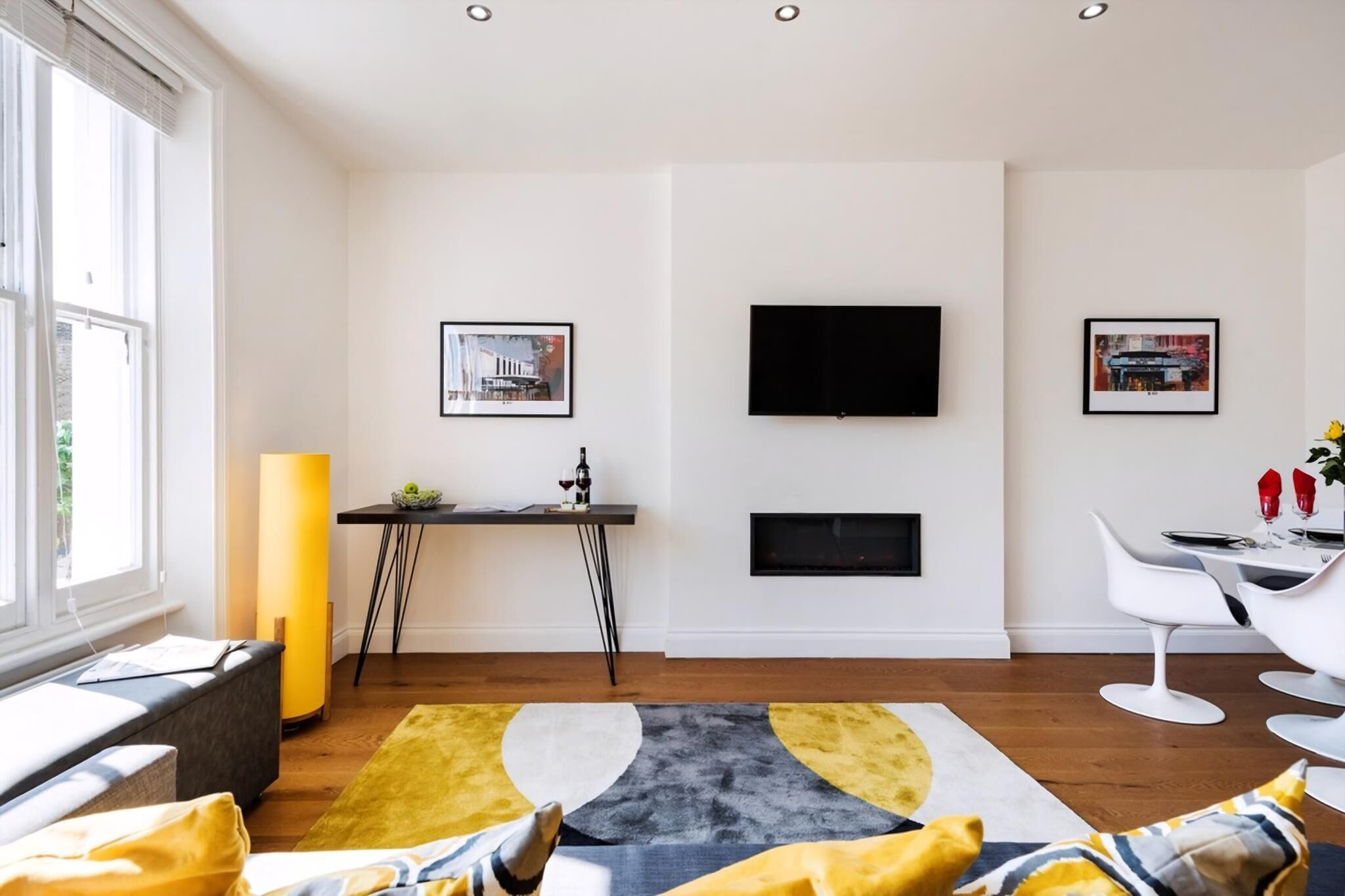 Ett modernt vardagsrum med en soffa, ett soffbord, en öppen spis, en tv och inramade konstverk på väggarna.