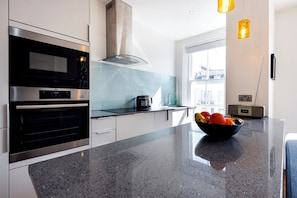 A modern kitchen with stainless steel appliances, a black countertop, and a bowl of fruit.